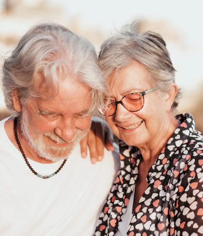 Happy adult mature beautiful senior couple of grandparents hug sitting in outdoors smiling carefree. Active caucasian elderly people white haired enjoying vacation at sea or retirement and free time